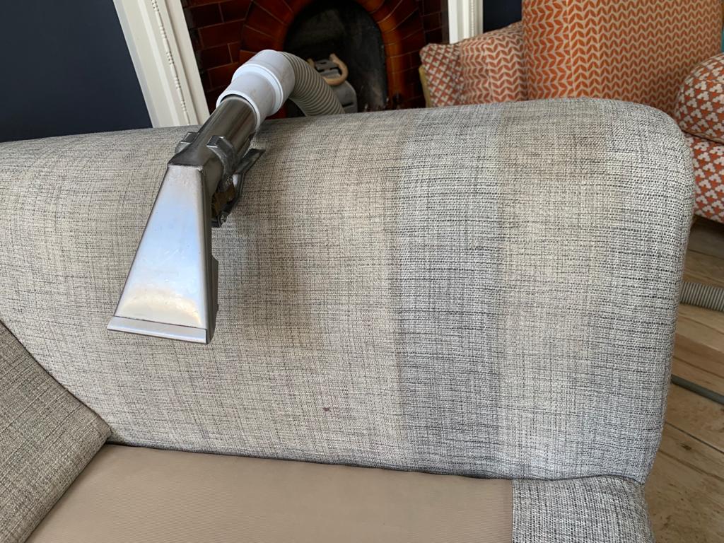 This is a photo of an arm of beige sofa that shows a test patch that has been steam cleaned. The steam cleaning machine is also showing in the photo works carried out by Chessington Carpet Cleaning