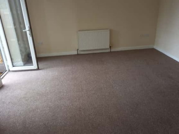 This is a photo of a living room after it has been cleaned. The room is empty and has a brown carpet that has been steam cleaned works carried out by Chessington Carpet Cleaning